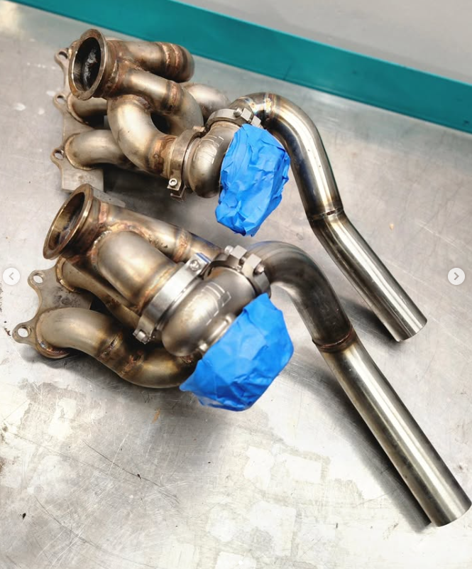 Twin Precision turbos on custom stainless manifolds with blue painter's tape over the inlets, before refresh — raw welds, no wastegates installed